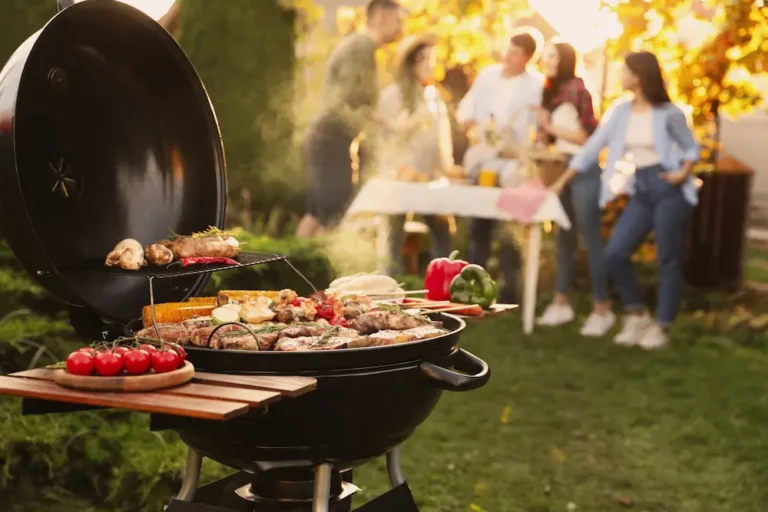 Outdoor backyard BBQ grill with food cooking and people gathered nearby.