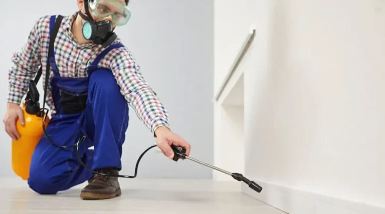Pest control professional applying treatment along an indoor baseboard