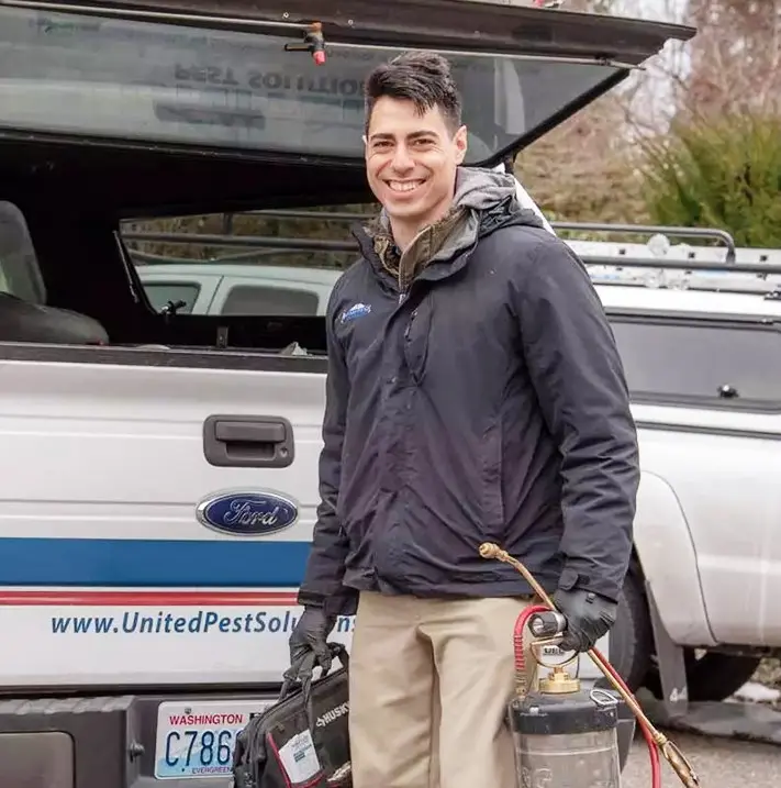 A united pest control technician behind his service vehicle happy to serve